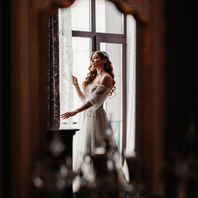 Невеста на свадебных сборах в номере гостиницы в отражении зеркала
